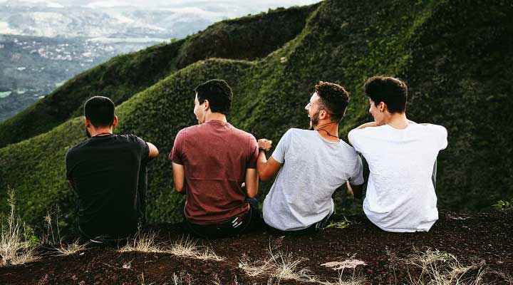 ۴ مرد درحال خنده نشسته روی تپه‌ای روبه کو‌های سبز نشانی از دوستی‌های مردانه